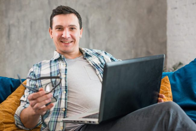 Photo of smiling man with laptop illustrates blog: "4 Reasons to Refinance Your Business Loan"