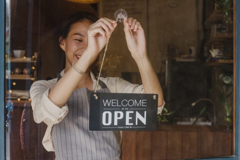 Photo of girl hanging a sign that reads "open" illustrates blog: "Can SBA Loans Be Used To Start a Business?"