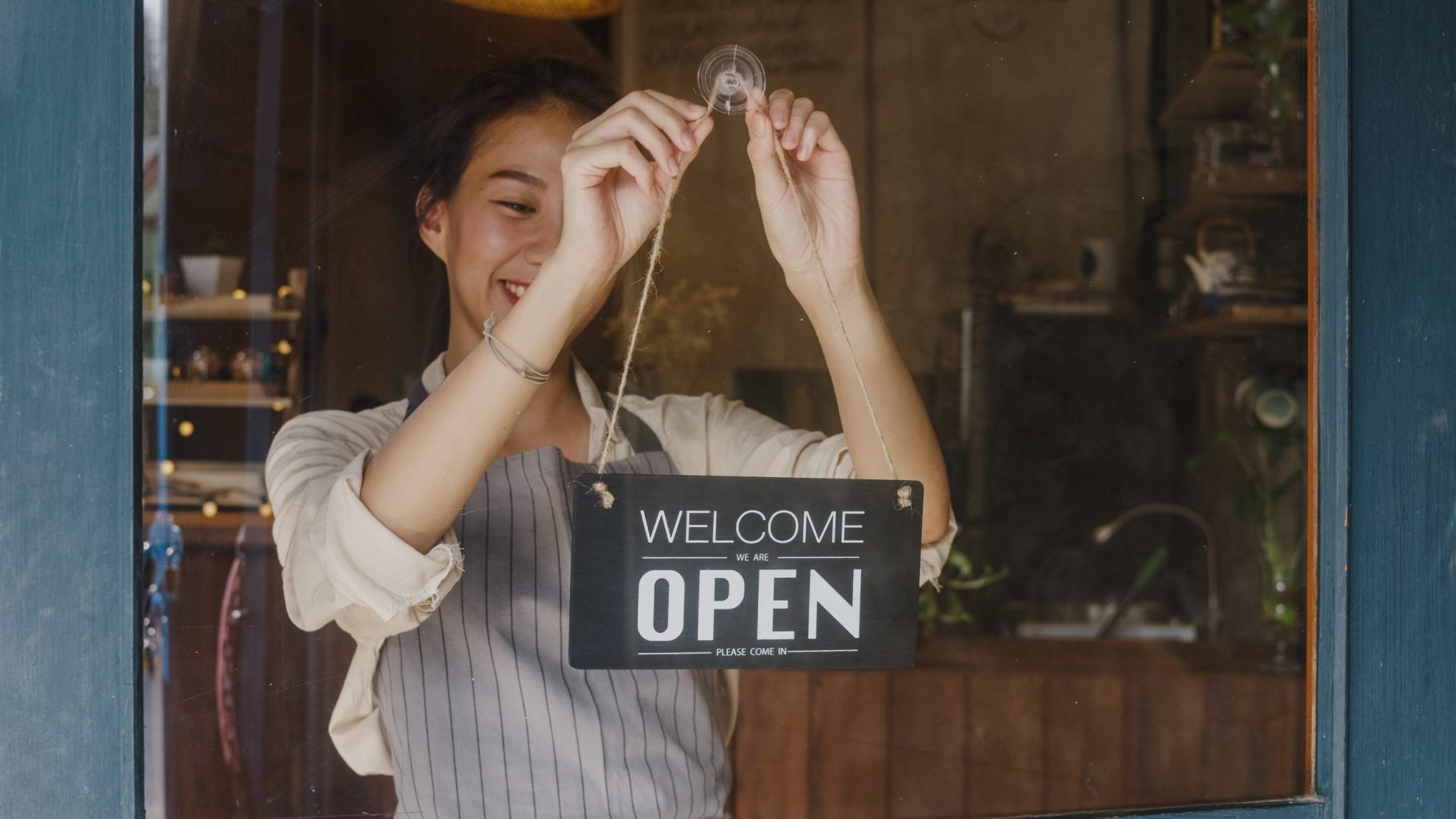 Photo of girl hanging a sign that reads "open" illustrates blog: "Can SBA Loans Be Used To Start a Business?"