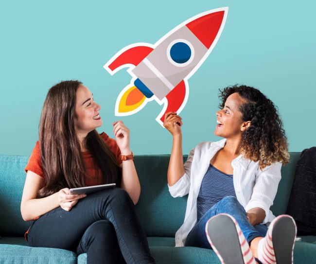 Two smiling women looking at cardboard rocket illustrate blog "What’s the Best Loan for Starting a Business?"