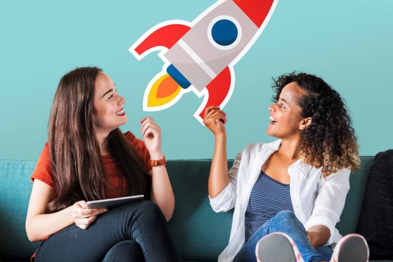 Two smiling women looking at cardboard rocket illustrate blog "What’s the Best Loan for Starting a Business?"