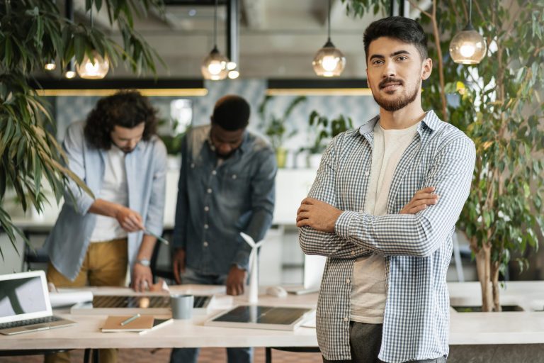 Man with crossed arms with to men talking in the background illustrates blog "4 Tips to Manage Business Finances"