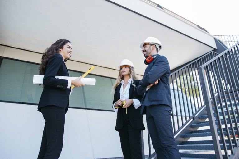 Two women and a man in hardhats with one of the women with a blueprint tucked under her arm illustrate blog "Can You Use an SBA 504 Loan To Buy Land?"