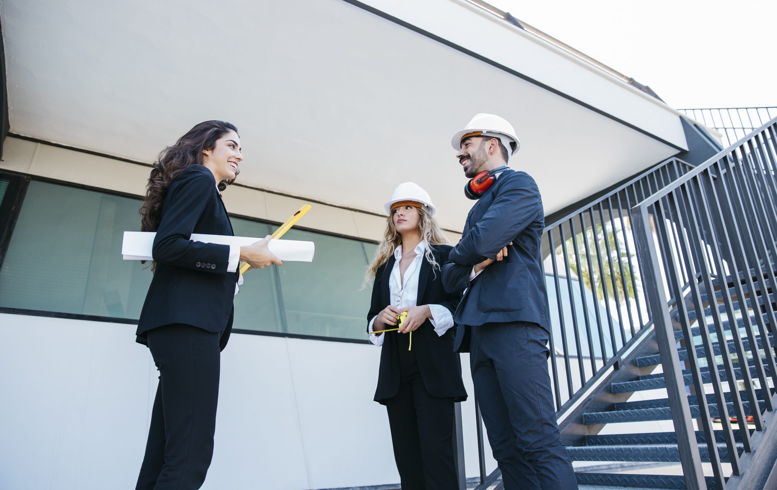 Two women and a man in hardhats with one of the women with a blueprint tucked under her arm illustrate blog "Can You Use an SBA 504 Loan To Buy Land?"